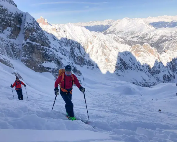 Sciatori scendono da un ripido pendio innevato sul Monte Cristallo, con vette maestose sullo sfondo. La **funivia** è lontana, ma l'avventura è appena iniziata.