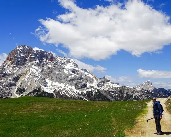 Un uomo con bastoncini da trekking su un sentiero in Trentino, con imponenti montagne innevate sullo sfondo. Un'esperienza di trekking trentino facile e panoramica.