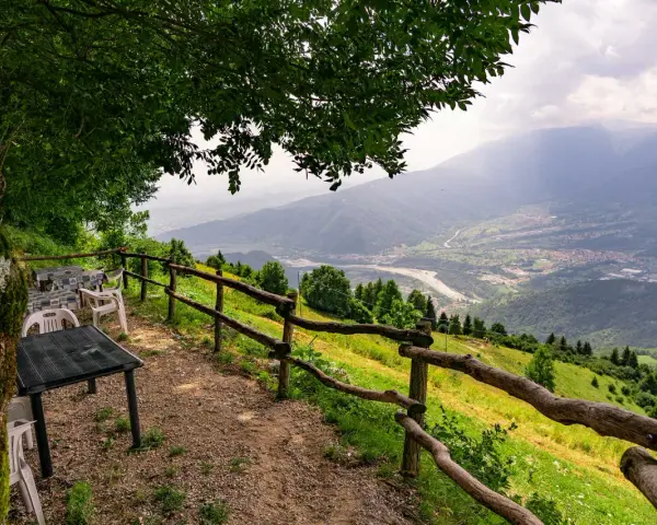Tavoli e sedie sotto un albero offrono una vista panoramica sulla valle dalla malga Molvine Binot.