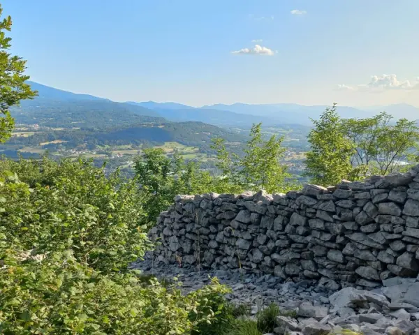 Muro di pietra a secco con vista panoramica su una valle alpina e montagne all'orizzonte.