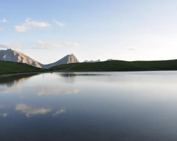 Sestriere estate: un lago alpino riflette le montagne e il cielo azzurro, un'oasi di pace.