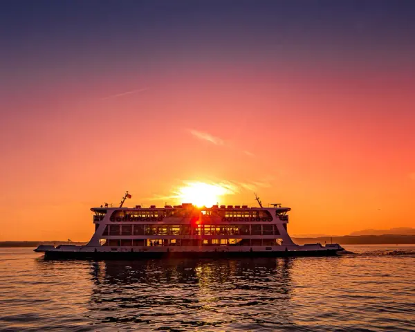 Traghetto in navigazione sul Lago di Garda al tramonto, con il sole che illumina il cielo e il riflesso sull'acqua.