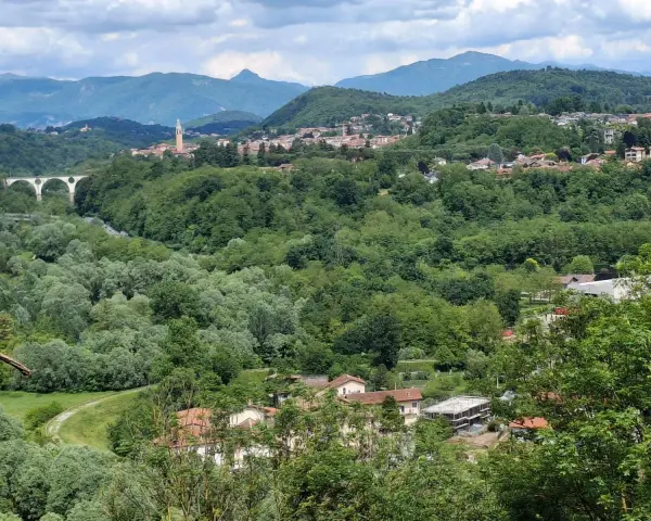 Panoramica collinare con un ponte ad archi, un campanile e case sparse a Cassano Magnago, circondata da rigogliosa vegetazione.