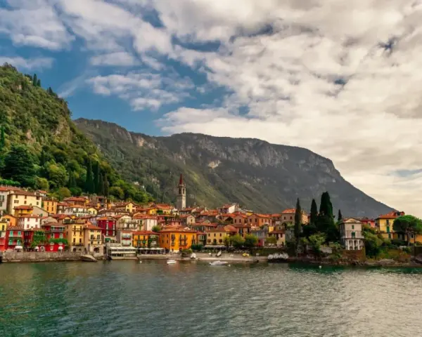 Colorate case affacciate sul lago di Lecco, con montagne verdi sullo sfondo e un cielo nuvoloso.