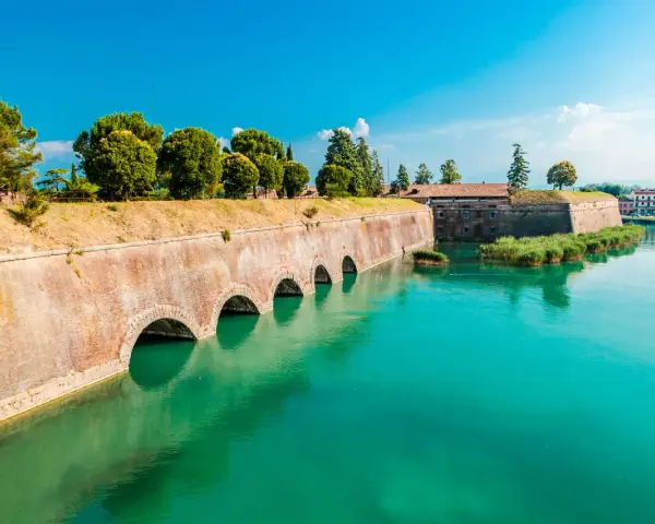 Fortificazioni storiche con archi in mattoni e acqua turchese, dove si trova Peschiera del Garda.