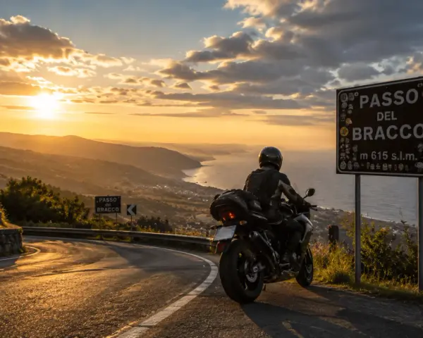 Motociclista al Passo del Bracco al tramonto, con vista sul mare e sulle colline illuminate dalla luce dorata.
