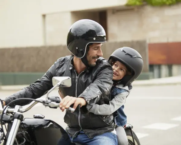 Padre e figlio sorridono in moto, rispettando il nuovo codice della strada per bambini in moto.