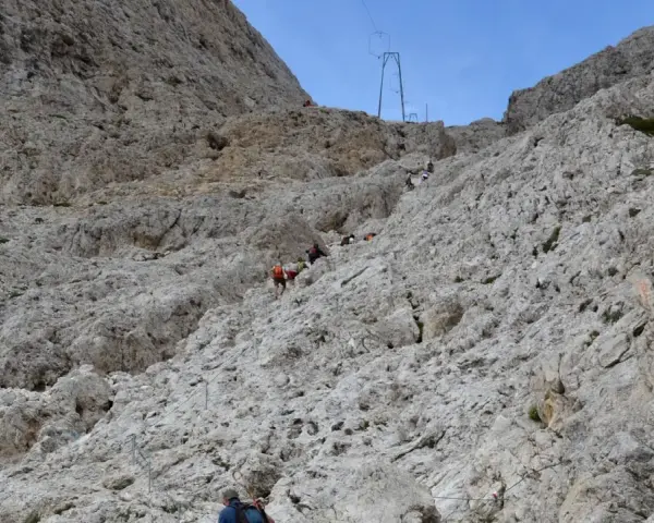 Escursionisti affrontano la **difficoltà** del sentiero verso il **Rifugio Re Alberto**, aggrappandosi a cavi d'acciaio su un ripido pendio roccioso.