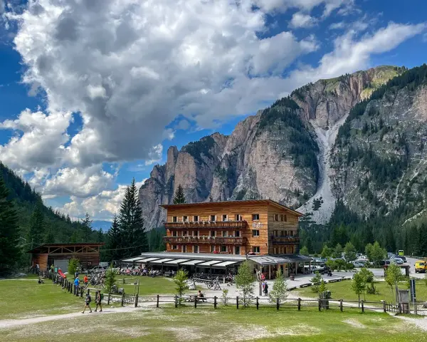 Edificio in legno a Pederu San Vigilio, con montagne imponenti e cielo nuvoloso.