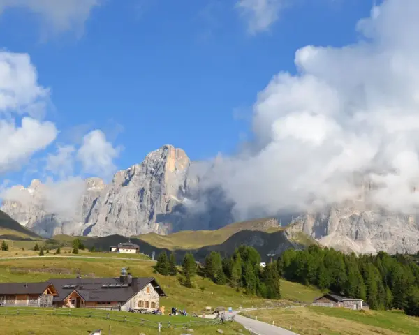 Panorami mozzafiato al Passo Rolle: malghe, boschi e vette imponenti sotto un cielo azzurro con nuvole bianche.