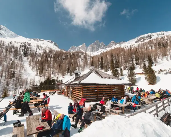 Malga Valcigolera, un rifugio alpino innevato con gente seduta ai tavoli. Per sapere come arrivare, guarda l'immagine.