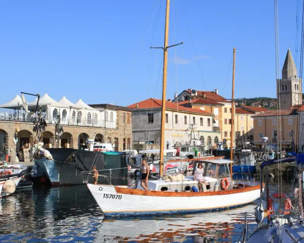Porto di Muggia cosa vedere: barche a vela, edifici storici e un campanile svettano sotto il cielo azzurro.