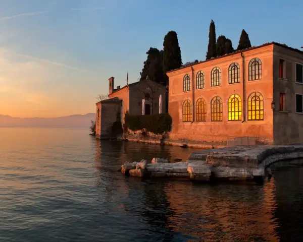 Punta San Vigilio: un tramonto dorato illumina la spiaggia e l'antica villa affacciata sul lago.