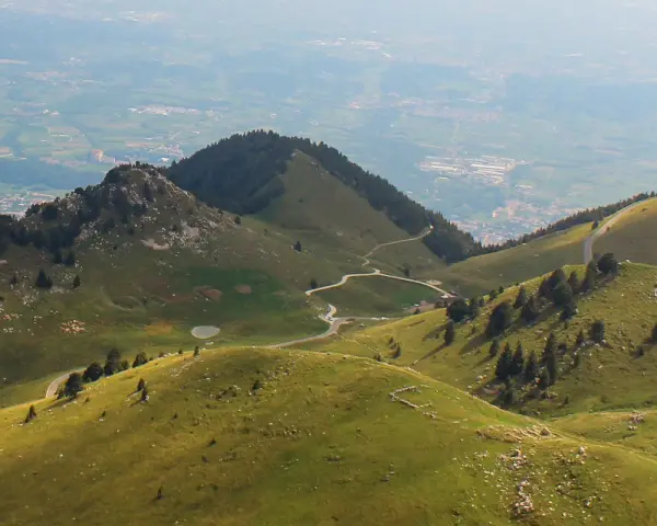 Panorami verdi con strade tortuose e malghe sul Monte Grappa. Un gregge pascola vicino a un piccolo lago.