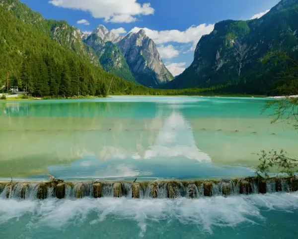 Splendido lago turchese incastonato tra montagne verdi, ideale per una toblacher see wanderung. Una cascata artificiale crea un effetto scenografico.