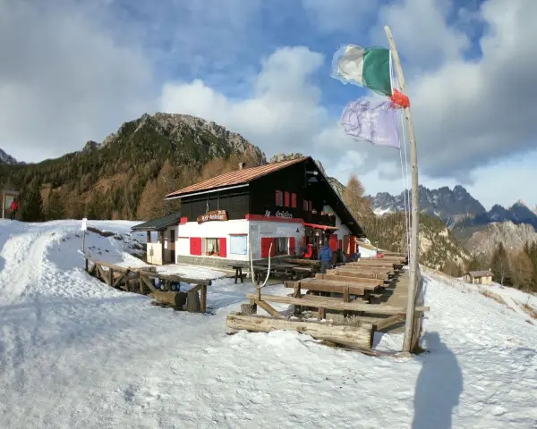 Rifugio Antelao innevato, con tavoli esterni e bandiere. Informazioni su come arrivare al rifugio sono visibili.