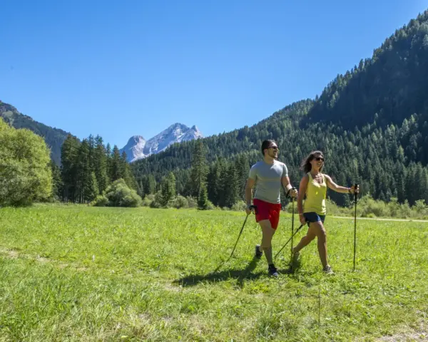 Coppia fa nordic walking in un prato verde con montagne sullo sfondo, ideale per canazei escursioni facili.