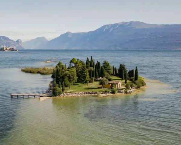 Un'incantevole isola dei conigli sul Lago di Garda, con un piccolo molo e una casetta gialla tra i cipressi.