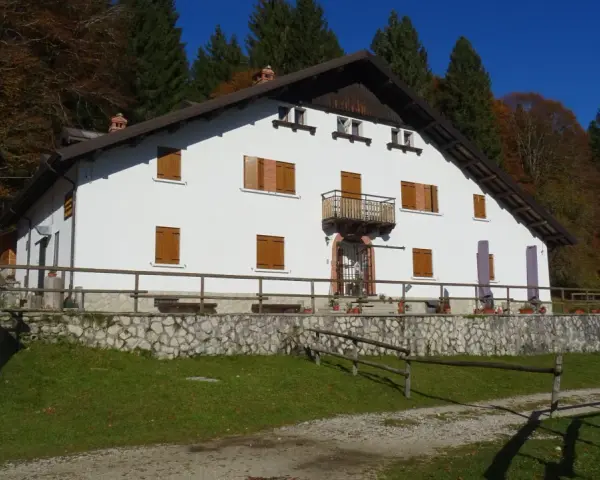 Il rifugio Città di Vittorio Veneto, immerso nel foliage autunnale, accoglie con la sua facciata bianca e le finestre con persiane in legno.