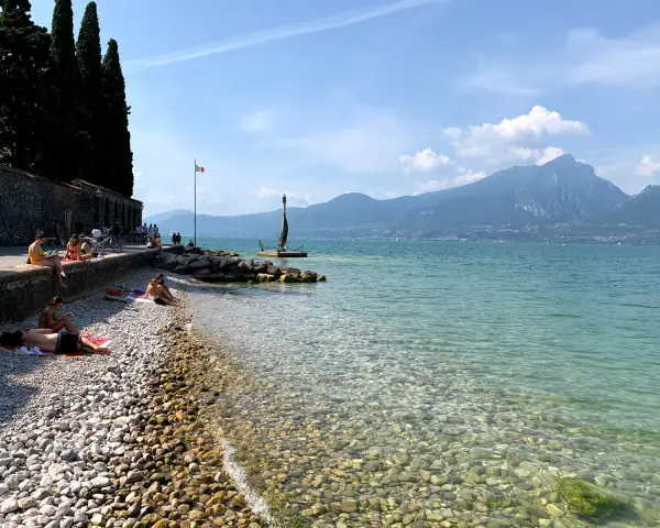 Persone rilassate sulla torri del benaco spiaggia, con acque limpide e montagne sullo sfondo.