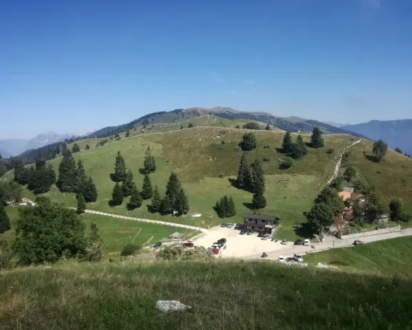 Panorami verdi e dolci colline del Pian delle Femene, con un rifugio e parcheggio.