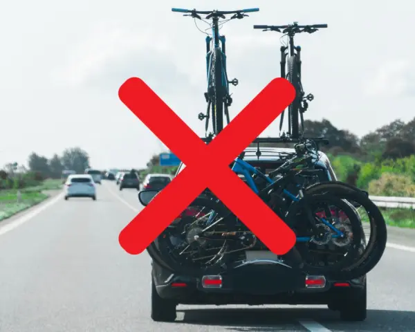 Attenzione al carico sporgente auto! Biciclette sul portabici posteriore, ma una grande X rossa indica un problema di sicurezza.