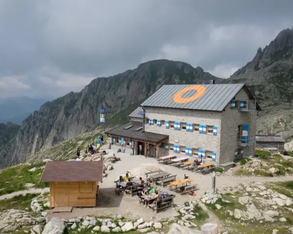 Il rifugio Cima d'Asta, con le sue finestre blu e arancioni, accoglie escursionisti tra rocce e montagne nebbiose.