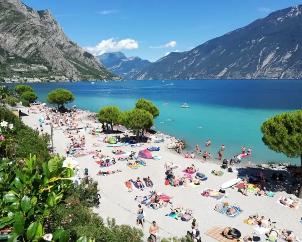 Una vivace spiaggia di Limone sul Garda, con gente che prende il sole e nuota nelle acque turchesi del lago.