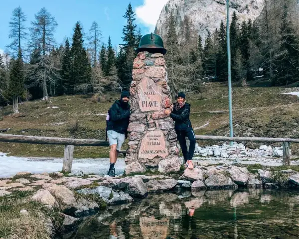 Coppia sorridente vicino a un monumento in pietra a Sappada, ideale per passeggiate facili.