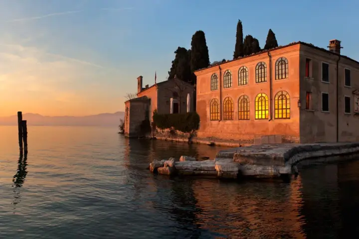 Punta San Vigilio: un tramonto dorato illumina la spiaggia e l'antica villa affacciata sul lago.