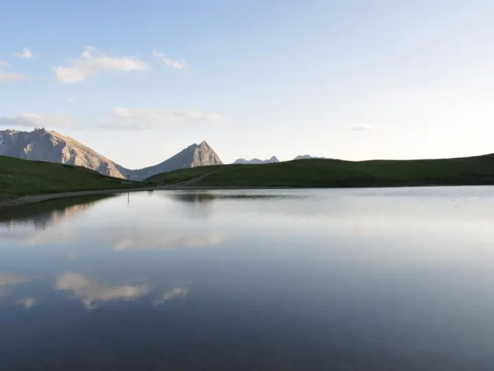 Sestriere estate: un lago alpino riflette le montagne e il cielo azzurro, un'oasi di pace.