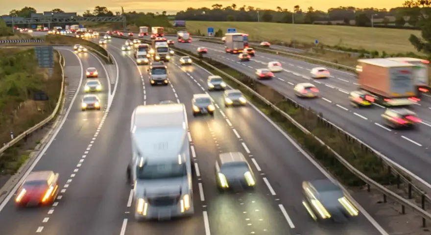 Traffico intenso su un'autostrada al tramonto. Auto e camion sfrecciano, creando scie luminose. Chissà se il limite velocità autostrada 150 dove è rispettato.