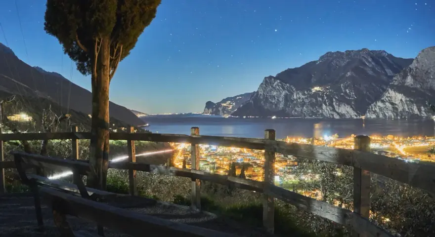 Peschiera del Garda di sera: un panorama mozzafiato con luci scintillanti, montagne imponenti e un cielo stellato. Ideale per una serata romantica.