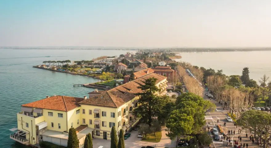 Vista aerea del centro storico di Sirmione, con edifici storici, lago e passeggiata affollata.