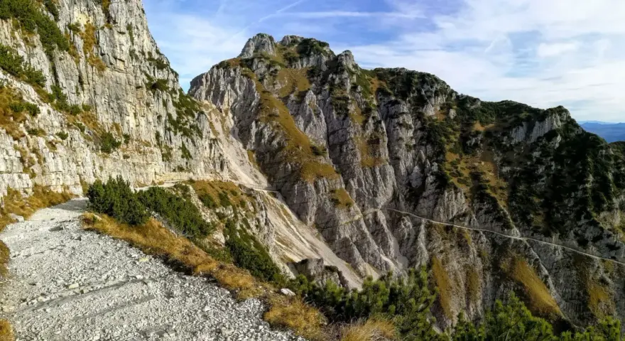 Sentiero roccioso in montagna, parte della strada degli eroi anello, con vegetazione sparsa e cielo azzurro.