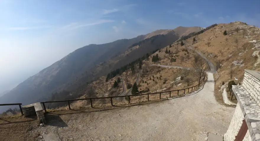 Strada tortuosa sul Monte Palon, Grappa, con vista panoramica sulle montagne e cielo azzurro.
