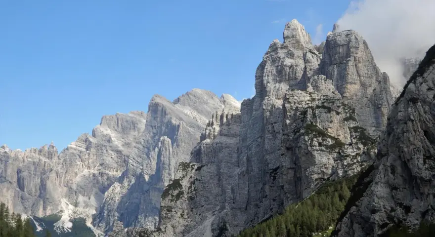 Imponenti cime rocciose dei monti di Framont si stagliano contro un cielo azzurro, con foreste di conifere ai loro piedi.