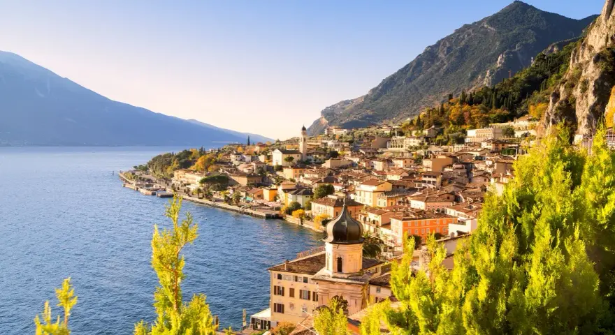 Un perfetto weekend sul lago di Garda: borgo colorato affacciato sull'acqua blu, montagne verdi e cielo limpido.
