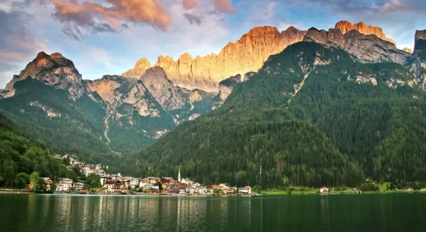 Un incantevole giro del lago di Alleghe, con il paese incastonato tra boschi e montagne maestose illuminate dal sole al tramonto.