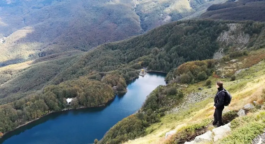 Un escursionista ammira il lago Santo Modenese, circondato da boschi autunnali e montagne.