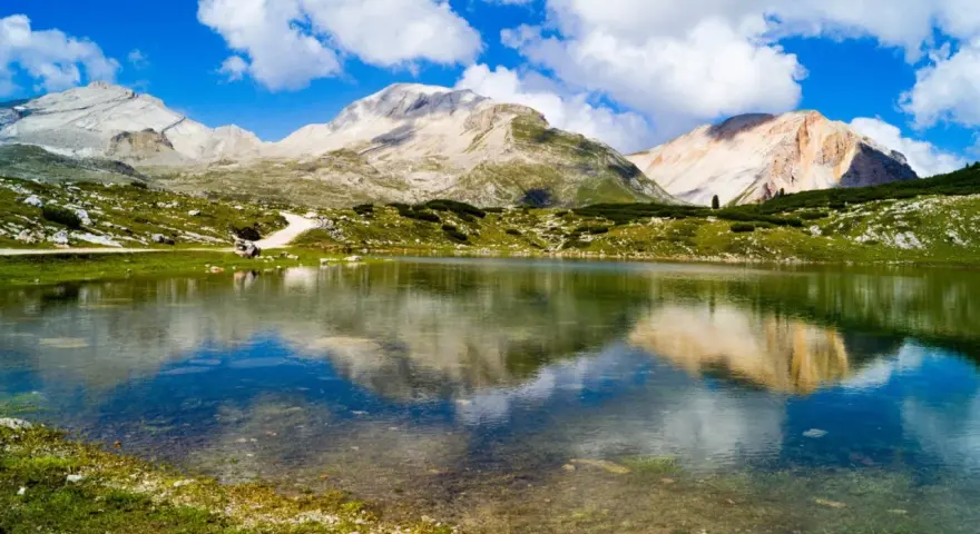 Un limpido lago di limo riflette montagne maestose e un cielo azzurro con nuvole bianche.