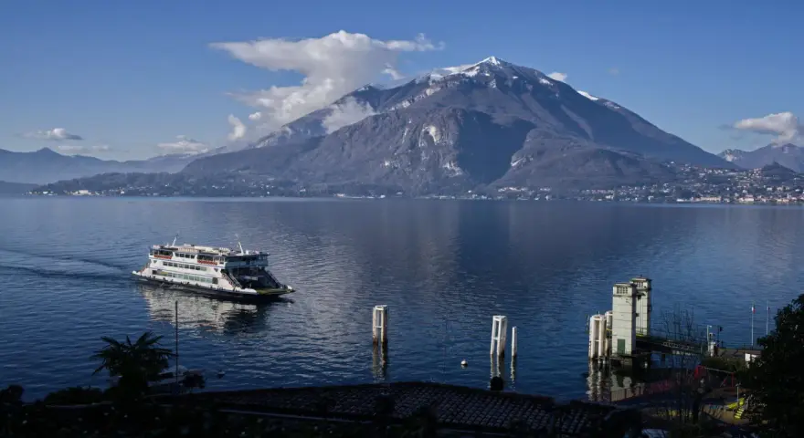 Traghetto sul lago di Como, con montagne innevate sullo sfondo e il pittoresco varenna centro storico.