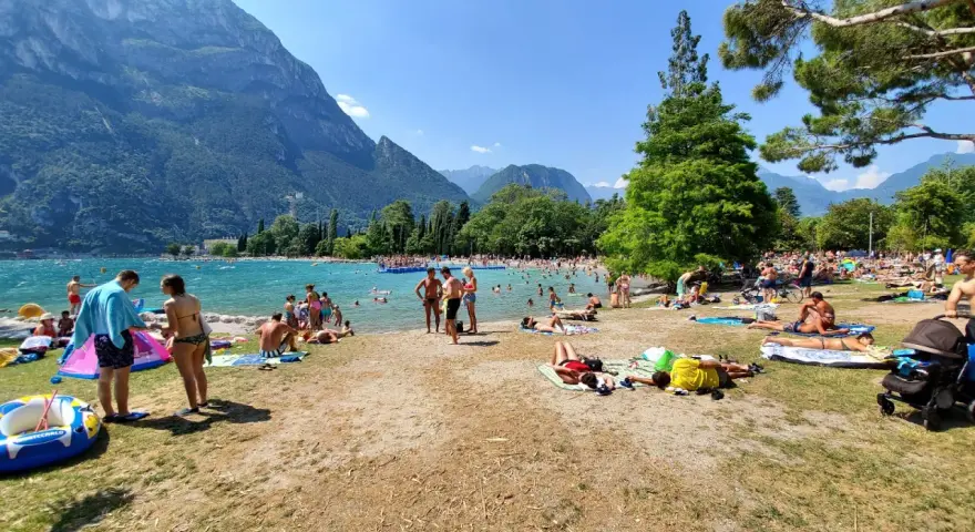 Spiaggia sabbioni Riva del Garda affollata di bagnanti sotto le montagne.