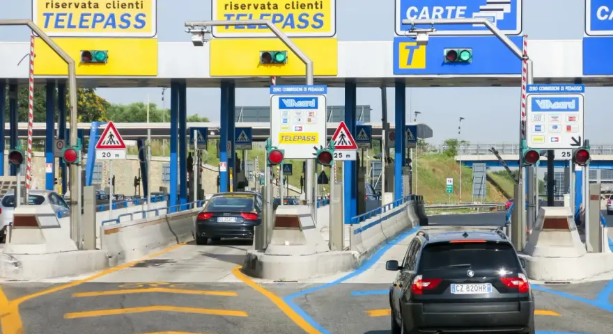 Casello autostradale con auto in coda. Segnaletica per Telepass e carte di credito. Possibile problema di mancato pagamento Telepass per un veicolo.