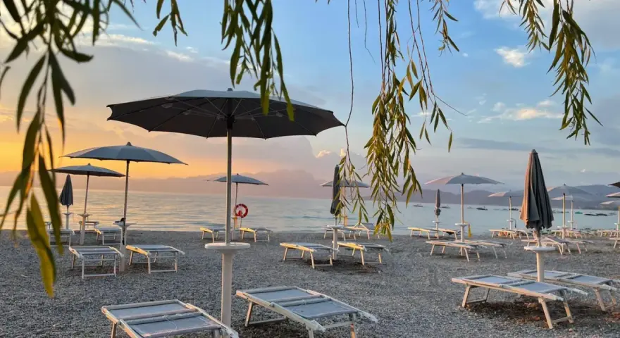 Alba sul lago di Garda, con lettini e ombrelloni pronti per accogliere i bagnanti sulle sue spiagge di sabbia.