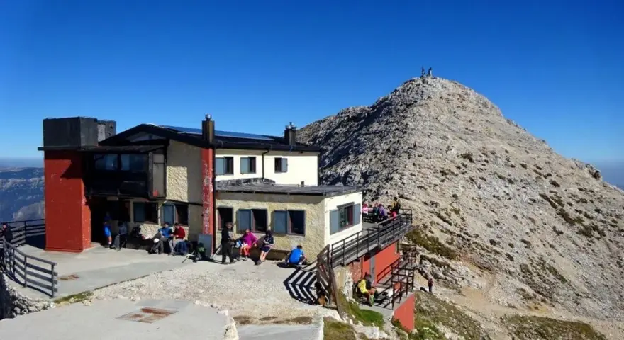 Rifugio Fraccaroli, un punto di ristoro in montagna. Per capire come arrivare, guarda la foto: un edificio con persone sedute all'esterno, con una vetta rocciosa sullo sfondo.