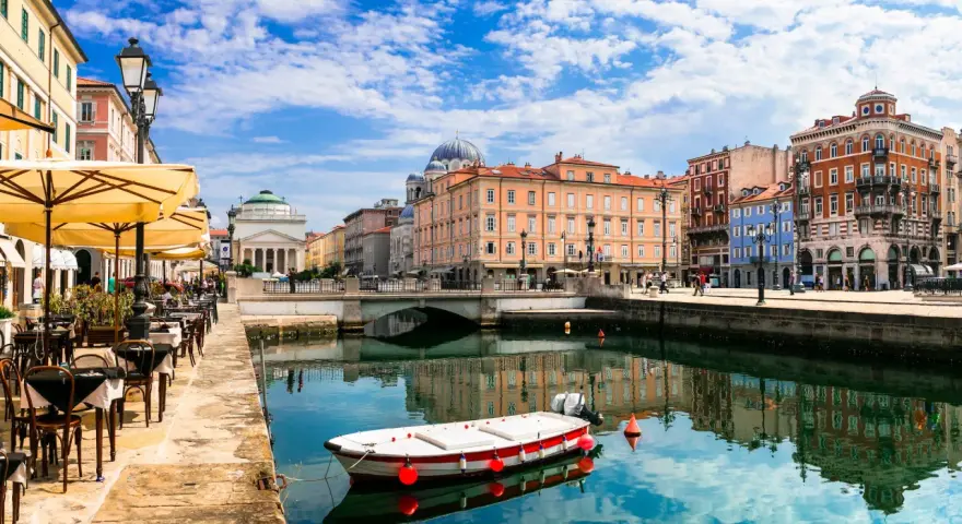 Un'incantevole vista di Trieste: un canale con una barca, caffè all'aperto e palazzi storici. Ecco cosa vedere a Trieste per un'esperienza indimenticabile.