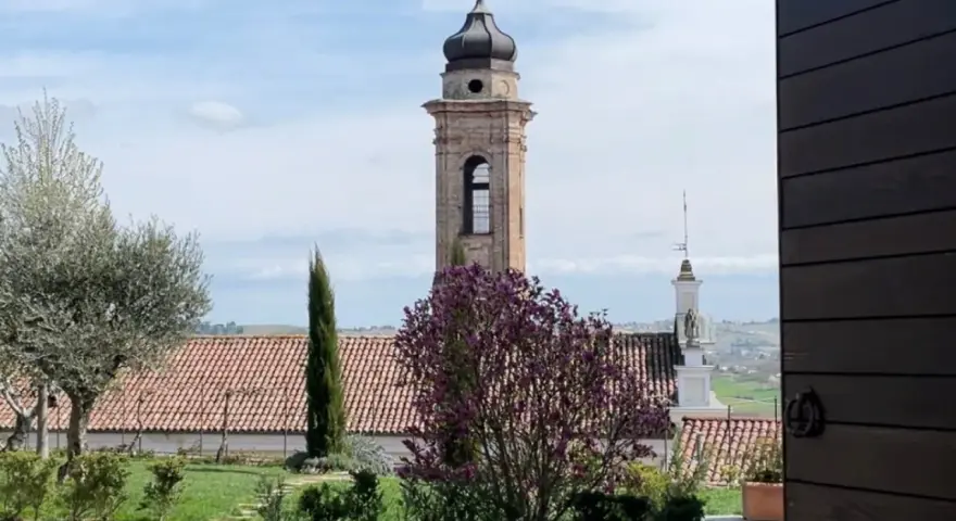 Torre campanaria e un albero in fiore, scorcio di un borgo tra le colline. Castagnole delle Lanze cosa vedere: un paesaggio incantevole.