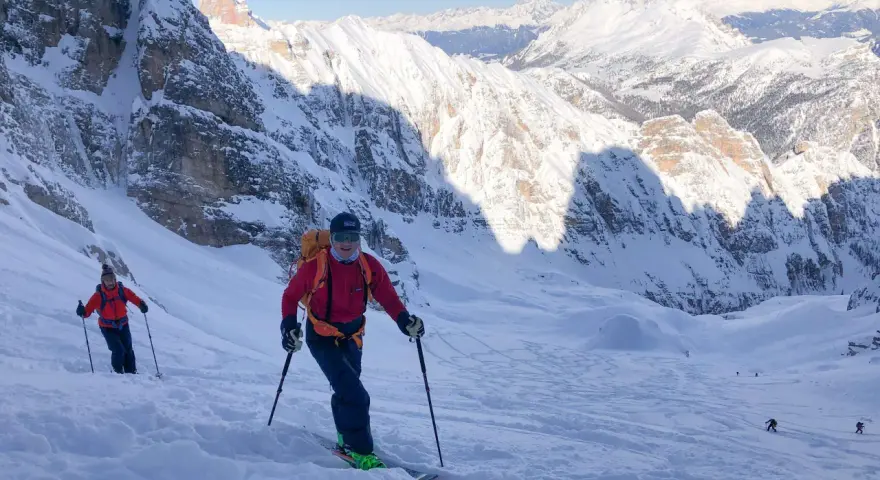 Sciatori scendono da un ripido pendio innevato sul Monte Cristallo, con vette maestose sullo sfondo. La **funivia** è lontana, ma l'avventura è appena iniziata.