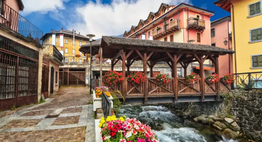Un pittoresco ponte di legno coperto, adornato di fiori, attraversa un torrente impetuoso. Un incantevole scorcio di cosa vedere in un borgo alpino.